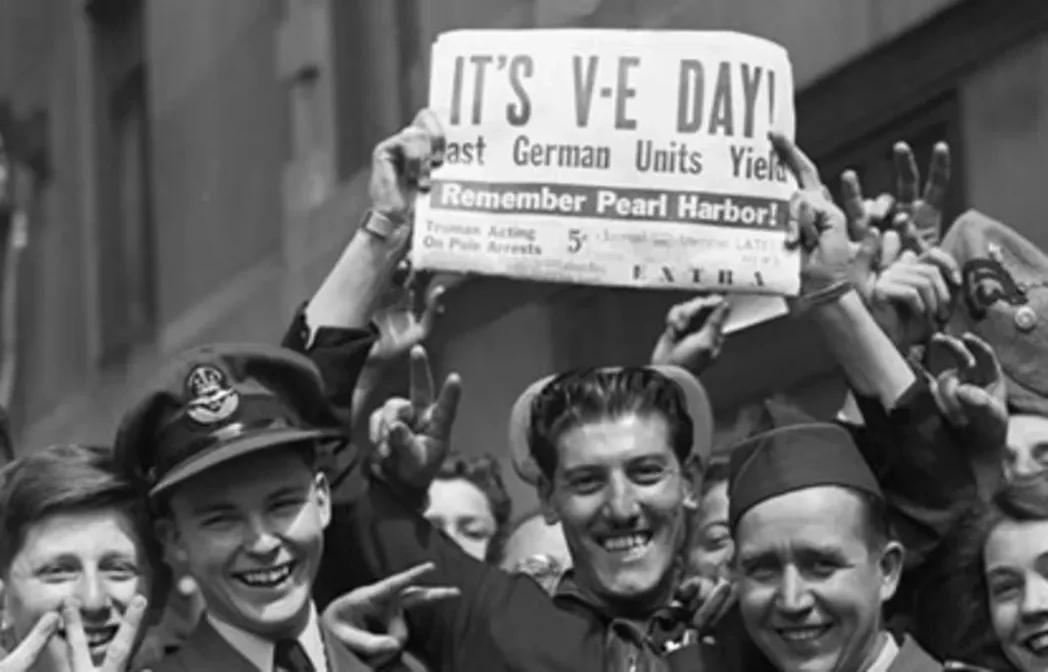 black and white photo from world war II of a group of soldiers and a sailor holding a newspaper announcing VE Day